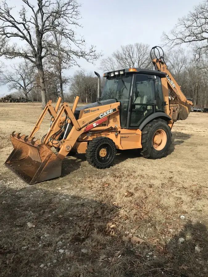 A yellow backhoe on a rural lot ready to dig