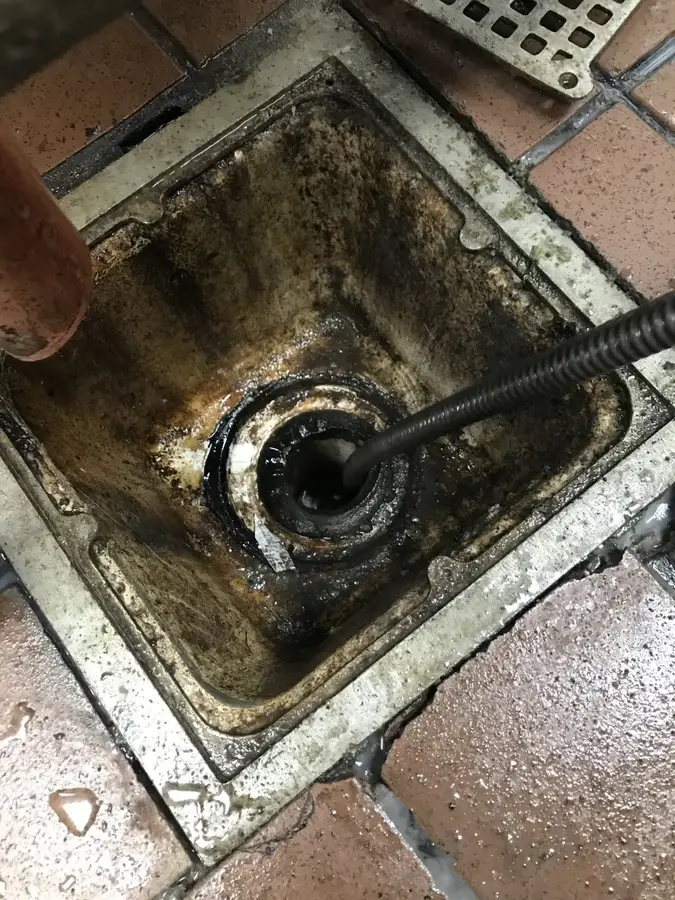 A drain cleaning cable running into a grimy commercial floor drain