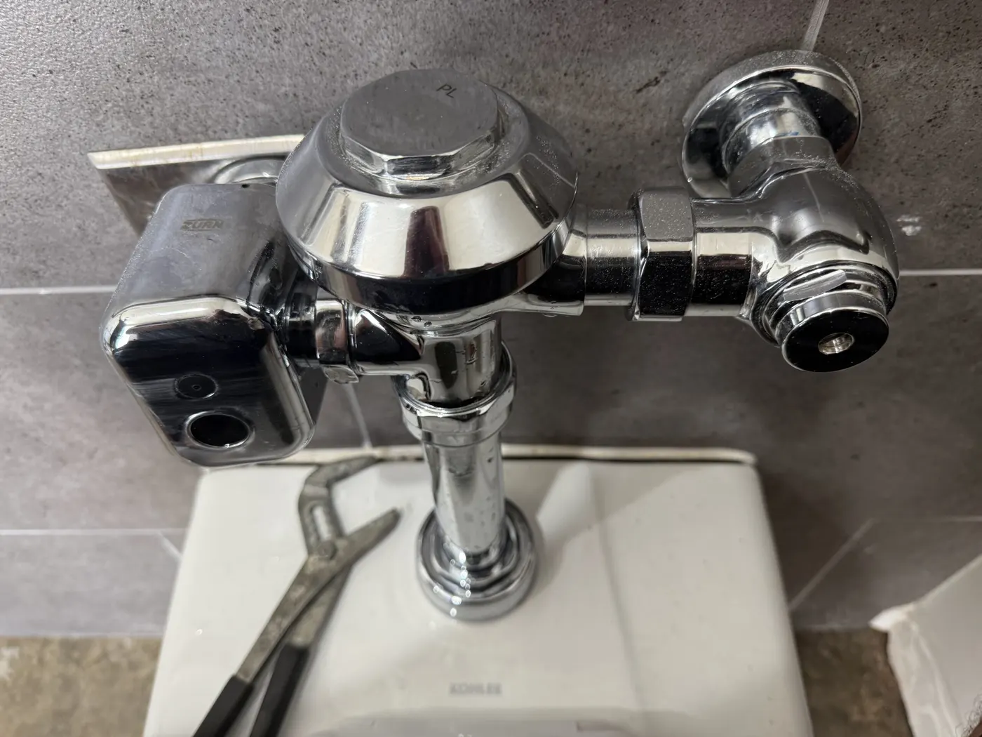 A chrome commercial flush valve installed on a wall-hung fixture