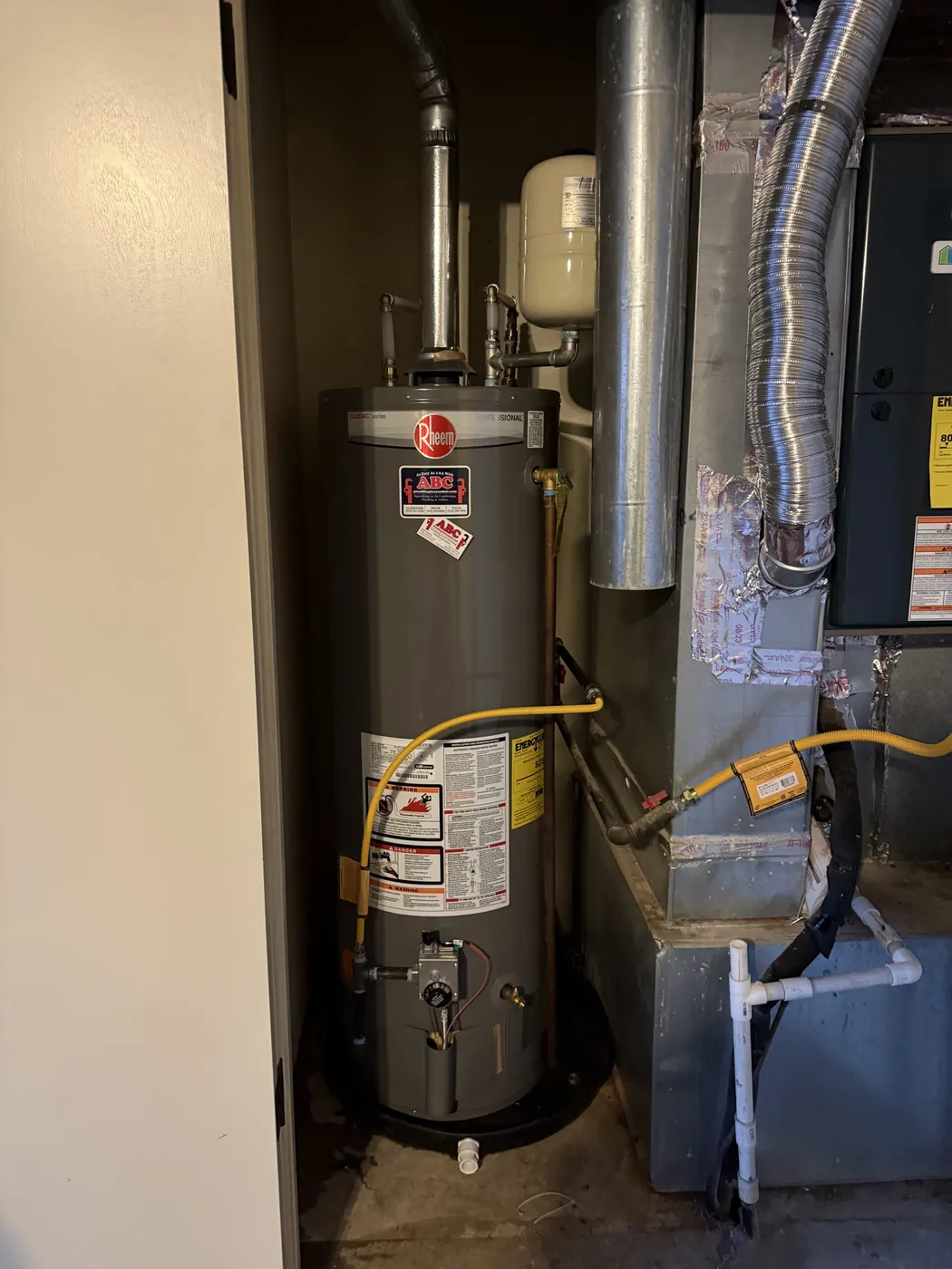 A gas water heater and furnace side by side in a utility closet with new venting