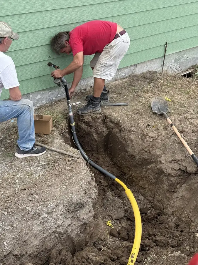 Two crew members connecting a new gas line in a trench beside a green house