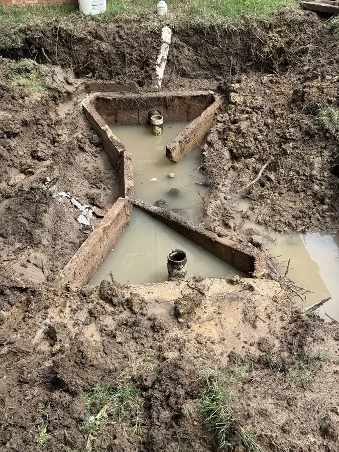 An opened septic tank inlet in a dug-out pit during a repair